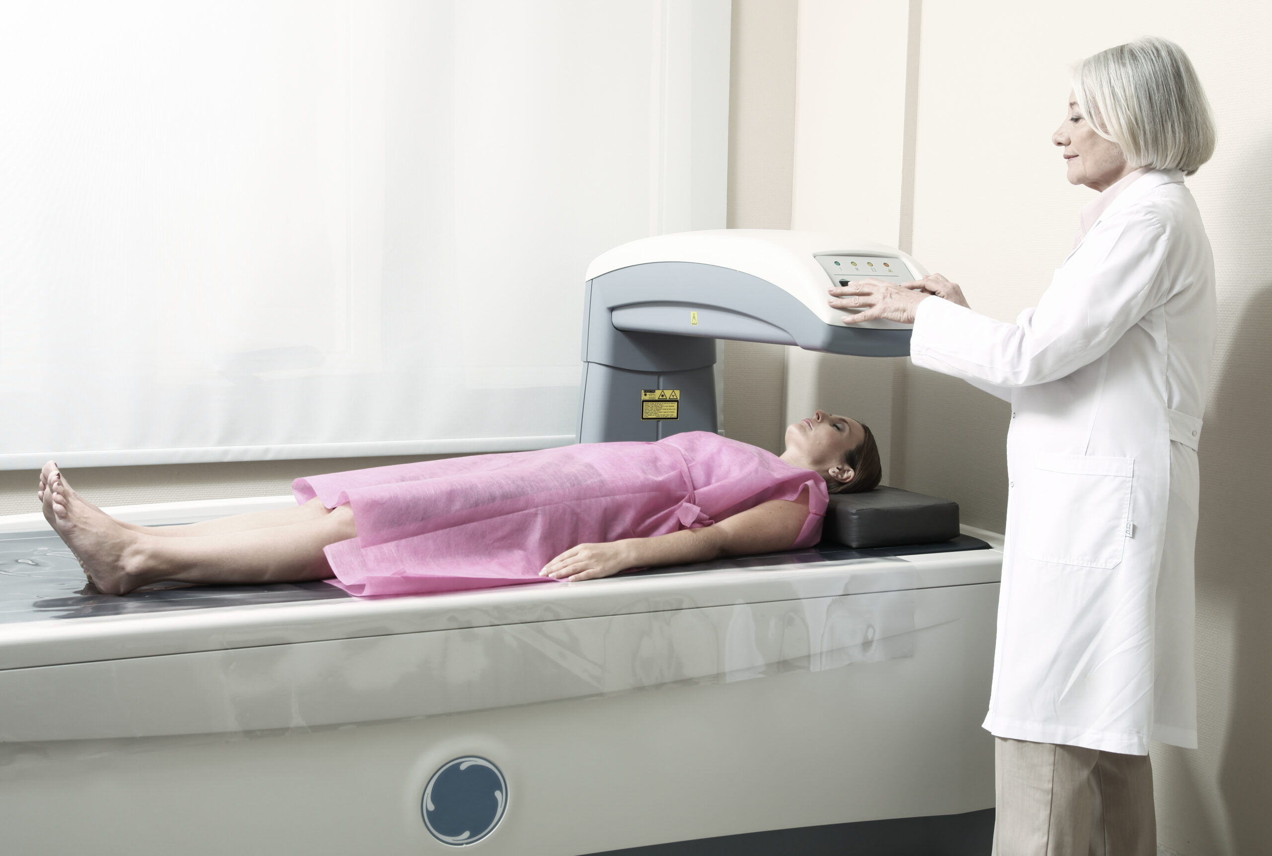 Female doctor examining woman in 40s at Bone Densitometer Machine.